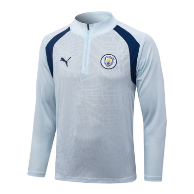 Camisola desportiva azul clara com detalhes azuis escuros, meio zip, logótipos Puma e Manchester City