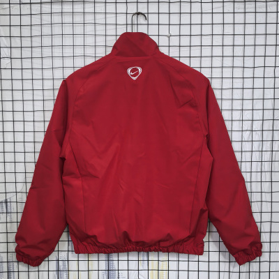 Casaco vermelho estilo bomber pendurado em cabide com fundo de rede preta.