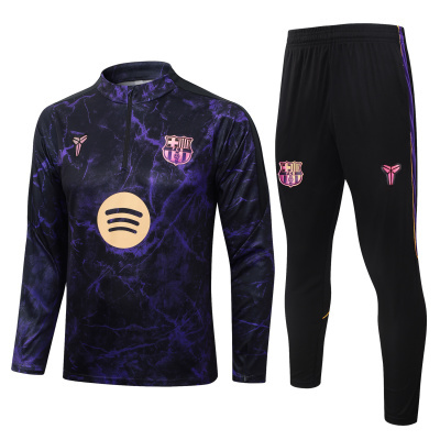 Conjunto desportivo com camisola roxa preta e calças pretas com emblemas FCB e logótipos.