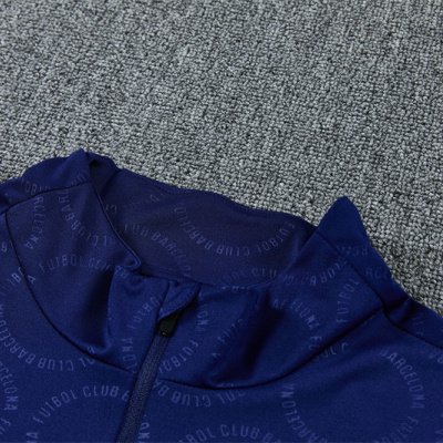 Peça de roupa azul escuro com fecho e texto FUTBOL CLUB BARCELONA com padrão em círculo