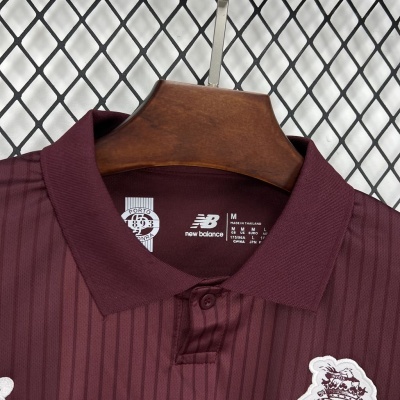 Polo bordô de riscas com logo bordado e gola com botão pendurado num cabide de madeira