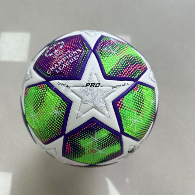 Bola de futebol branca com estrelas roxas, verdes e rosas com textos oficiais, sobre piso cinzento.