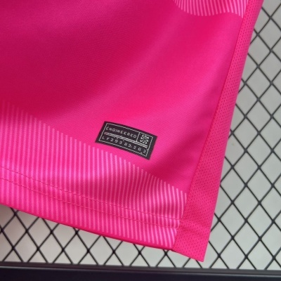 Peça de vestuário desportivo rosa com etiqueta ENGINEERED aproximada de fundo metálico em grelha.