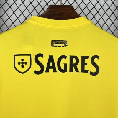 T-shirt amarela com logotipo preto SAGRES e ícone de elétrico no fundo de rede metálica