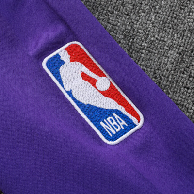 Tecido roxo com logotipo NBA bordado ao centro sobre tecido cinza trançado.
