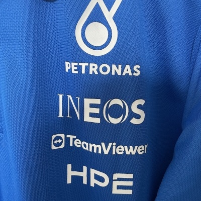 Pormenor de tecido azul com logos PETRONAS, INEOS, TeamViewer e HPE em branco