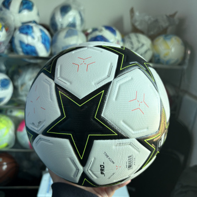 Bola de futebol branca com estrelas pretas e amarelas em fundo desfocado com várias outras bolas de futebol