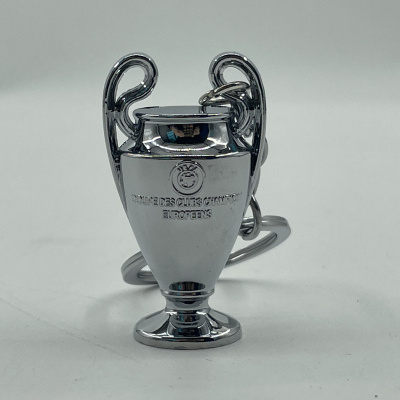 Chaveiro metalizado em forma de troféu com inscrições UEFA em fundo branco.