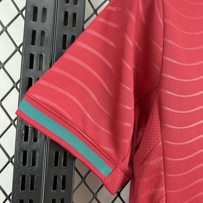 Manga de camisa vermelha com linhas e listra azul esverdeada na bainha pendurada em estrutura metálica preta