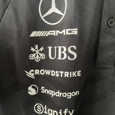 Polo preto com logótipos de marcas impressos em branco.
