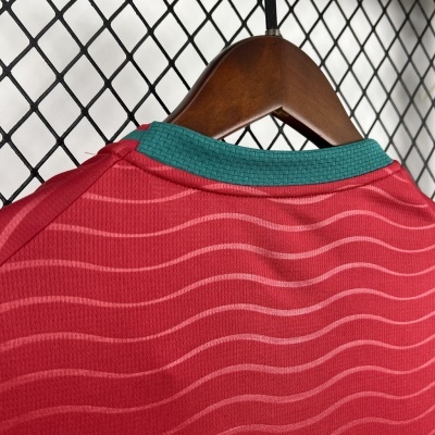 Camisola desportiva vermelha com padrão ondulado em tons claros e gola verde em cabide de madeira