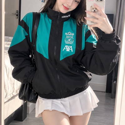 Mulher com casaco desportivo Adidas Liverpool e saia branca plissada a tirar selfie com smartphone.