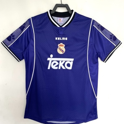 Camisola desportiva azul com gola em V preta e branca, logótipo Real Madrid e texto TEKA