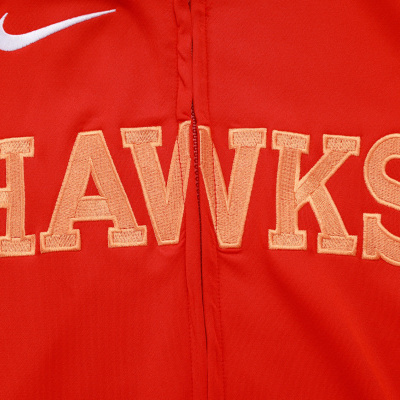 Pormenor de peça de vestuário vermelha com fecho e texto bordado HAWKS