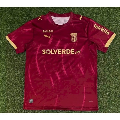 Camisola de futebol vermelha com detalhes dourados e logos de patrocinadores
