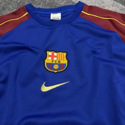 Camisola azul do FC Barcelona com detalhes vermelhos e amarelos e símbolo Nike dourado.