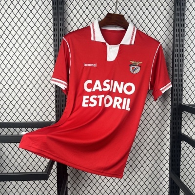 Camisola de futebol vermelha com gola branca e escrita CASINO ESTORIL, pendurada num cabide de madeira