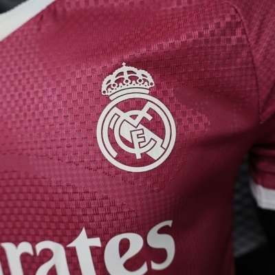 Camisola de futebol bordô com emblema branco do Real Madrid e texto parcial
