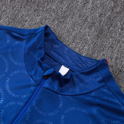 Camisola azul com padrão texto FUTBOL CLUB BARCELONA em círculos sobre tapete cinzento.