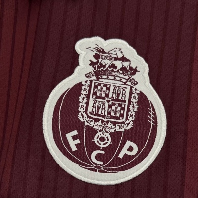 Emblema bordado branco de FC Porto em tecido borgonha com linhas verticais.