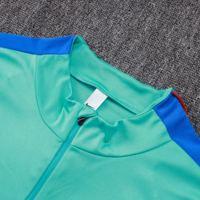 T-shirt desportiva verde água com detalhes azuis e vermelhos e logo Nike, sobre carpete cinzenta.