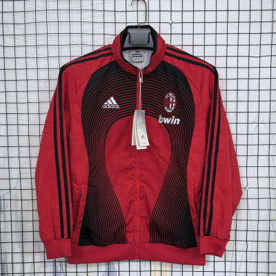 Casaco desportivo vermelho e preto com logotipos adidas, bwin e ACM 1899 pendurado numa grelha branca.