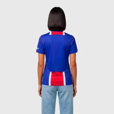 Pessoa com t-shirt desportiva azul, vermelha e branca e calças de ganga azuis vista de costas.