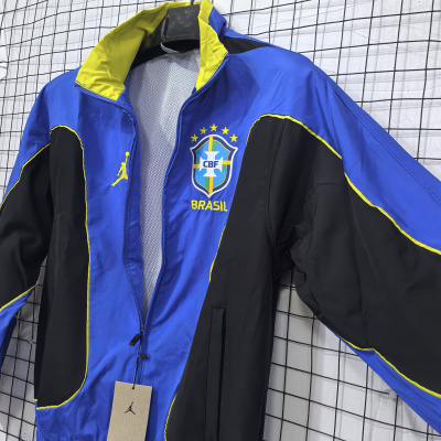 Casaco desportivo azul, preto e amarelo com emblema CBF Brasil, pendurado numa grelha metálica