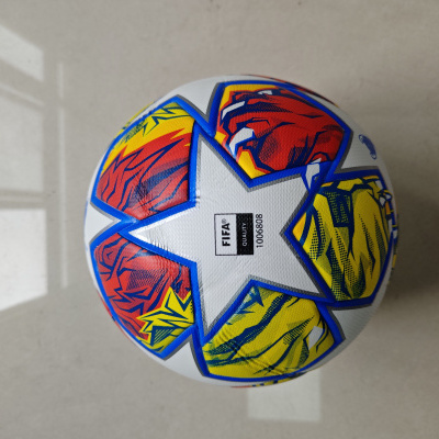 Bola de futebol branca com estrelas e detalhes coloridos sobre chão cinzento
