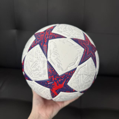 Bola de futebol branca com estrelas roxas e vermelhas apoiada numa mão