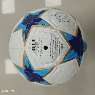 Bola de futebol branca com padrão azul e dourado e texto em várias línguas.