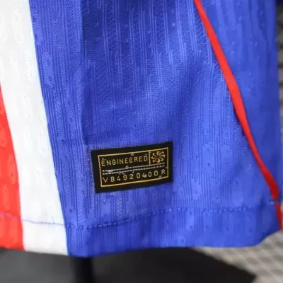 Etiqueta preta com texto dourado numa peça de roupa azul com detalhes em vermelho e branco