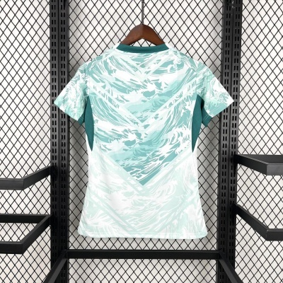 T-shirt desportiva verde água e branco com padrão abstrato pendurada em cabide de madeira numa estrutura metálica preta