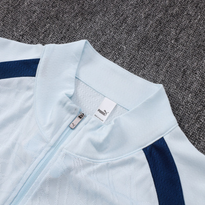 Casaco desportivo azul claro Puma com fecho zip e detalhes azuis escuros sobre superfície cinza.
