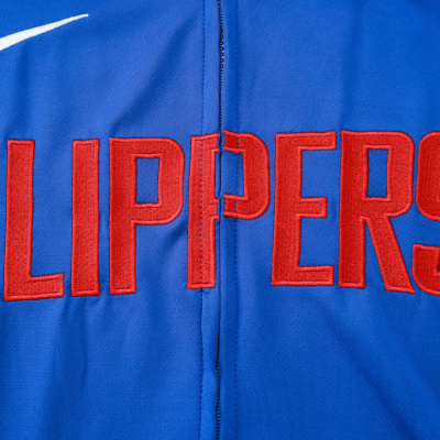 Peça de vestuário azul com fecho zip, texto CLIPPERS bordado a vermelho e logo Nike branca.
