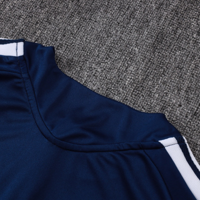Parte superior de roupa desportiva azul escuro com detalhes brancos sobre tapete cinza.
