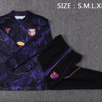 Conjunto de roupa desportiva roxo e preto com emblema FCB sobre tapete cinzento
