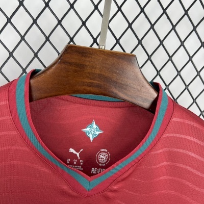 T-shirt desportiva vermelha com gola em V e detalhes em azul turquesa pendurada num cabide de madeira