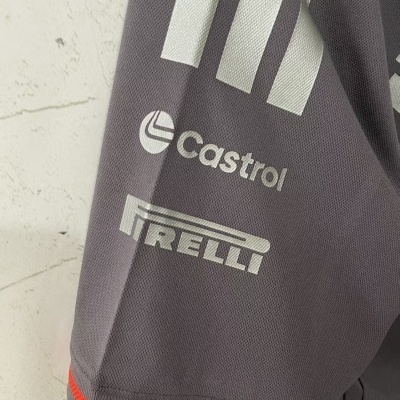 Detalhe de tecido cinzento com logos Castrol e Pirelli em branco e linha vermelha na bainha