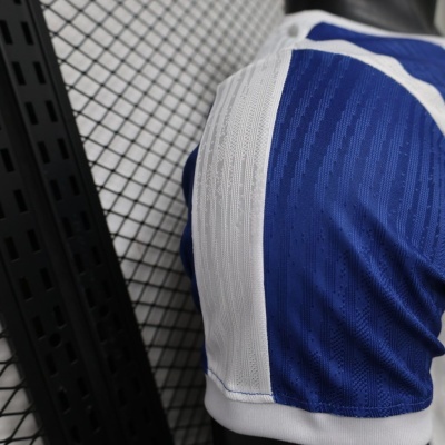 Calção desportivo azul e branco com padrão texturado junto a parede com grelha.