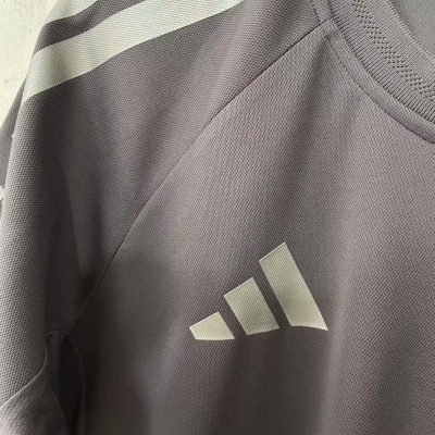 T-shirt desportiva cinza com riscas brancas no ombro e logótipo Adidas no peito.