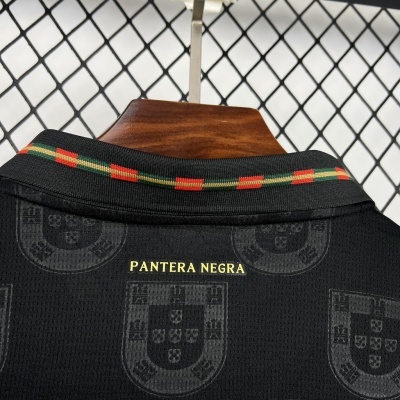 Camisola preta com padrão de escudos e texto PANTERA NEGRA na gola com riscas coloridas.