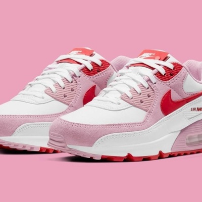 Ténis Nike Air Max brancos com detalhes rosa e vermelho sobre fundo rosa.