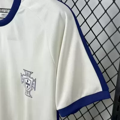 T-shirt branca com gola azul e emblema bordado no peito pendurada numa estrutura metálica negra