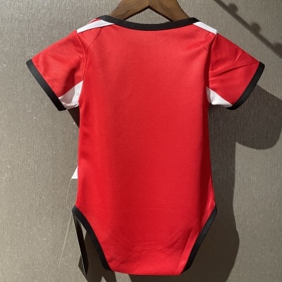 Body vermelho para bebé com detalhes pretos e brancos numa parede cinzenta.