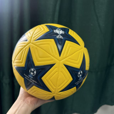 Bola de futebol amarela com estrelas negras e azuis e texto, segurada à mão