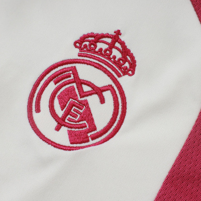Detalhe do emblema bordado do Real Madrid em tecido branco com parte de tecido vermelho ao lado.