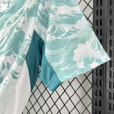 T-shirt desportiva verde água e branco com padrão abstrato pendurada numa estrutura metálica preta.