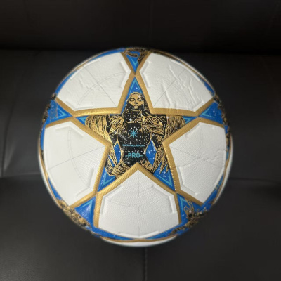 Bola de futebol branca com estrelas douradas e azuis com imagem de figura humana no centro