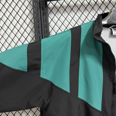Casaco adidas verde e preto pendurado em cabide metálico, fundo de malha metálica preta e branca.